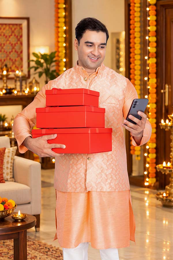 Indian man checking his smartphone while carrying festive gift boxes