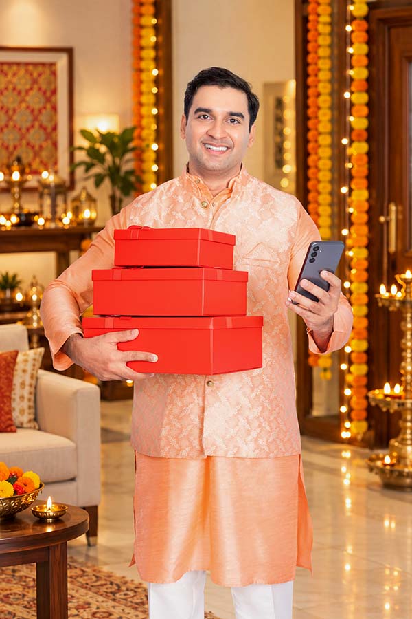 Smiling Indian man holding a smartphone and red gift boxes for Diwali