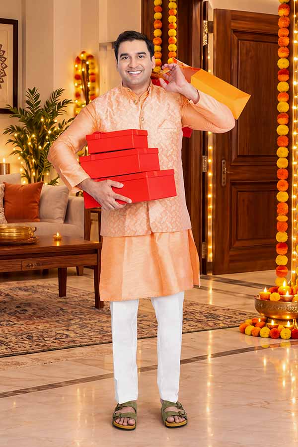 Indian man holding gift boxes and an orange shopping bag during a festival